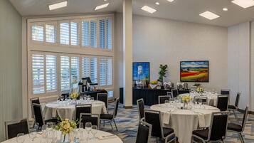 A conference room with round tables, chairs, and a large window with blinds.