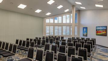 Un salón de conferencias con filas de sillas, ventanas amplias y luces en el techo.