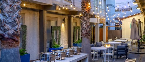 An outdoor seating area with tables and chairs, a fire feature, and string lights.