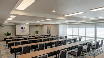 A conference room with multiple tables and chairs, ceiling lights, and a banner on the wall.