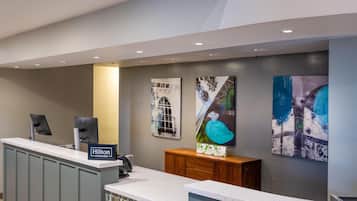 A hotel reception area with a counter, a desk, and a wall with artwork.