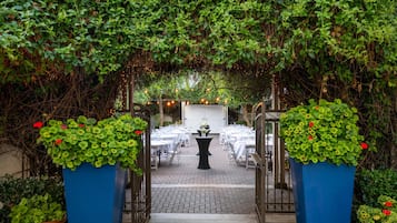 An outdoor dining area with tables and chairs, surrounded by greenery and a decorative archway.