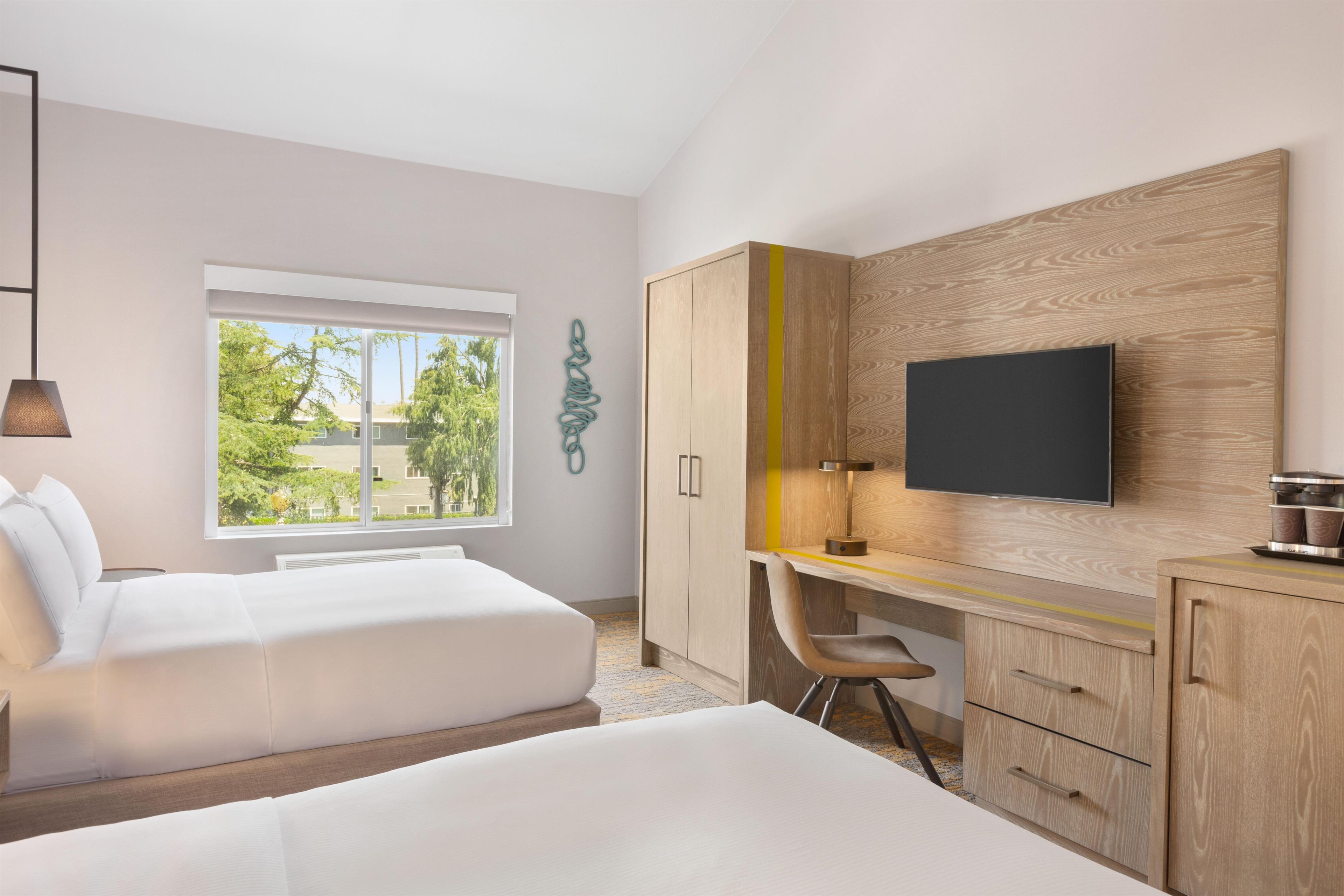 A modern hotel room with a bed, a desk, and a TV mounted on the wall.