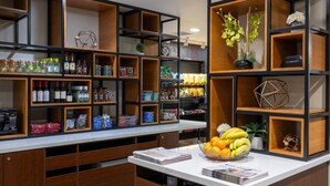 Zona de bar bien organizada con estantes llenos de bebidas, aperitivos y un bol de fruta en la encimera.