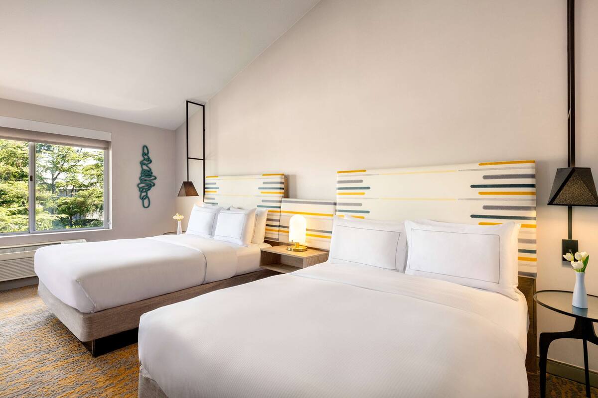 Quarto de hotel com duas camas, uma janela grande e um design moderno na parede.