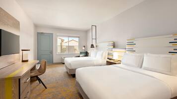 A hotel room with two beds, a desk, a chair, a TV, and a window with a view of buildings.