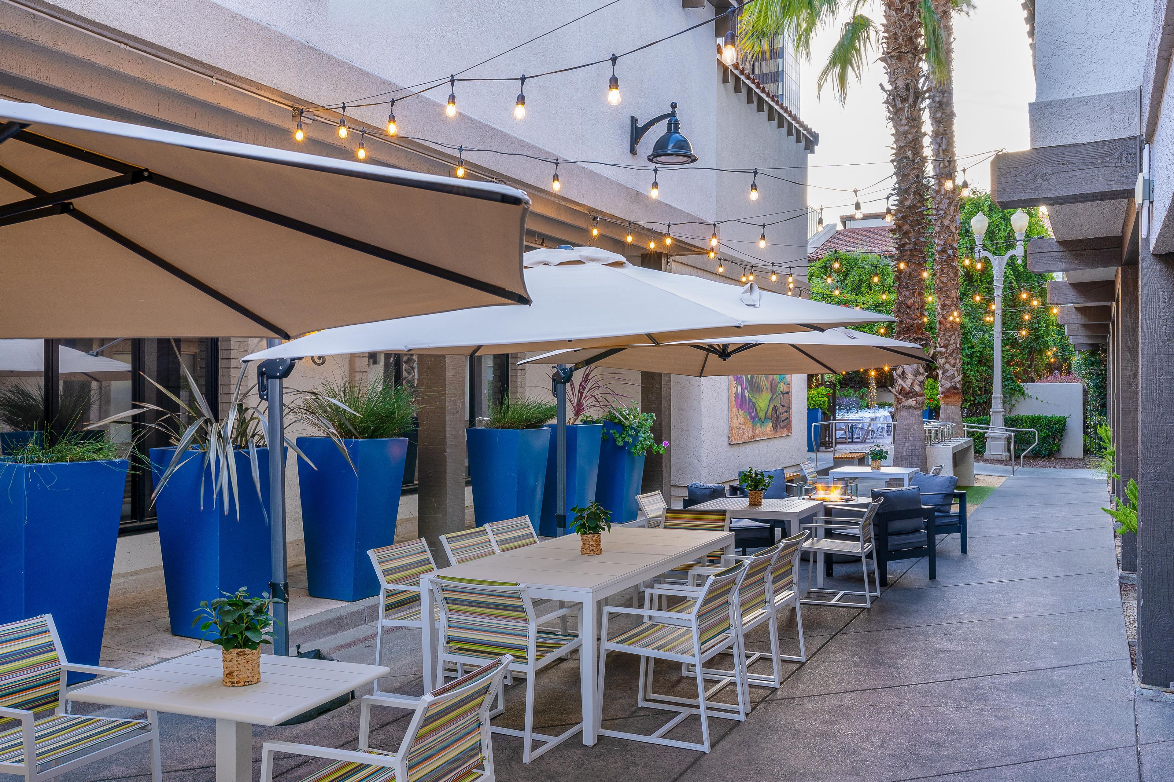 An outdoor patio with tables and chairs, string lights, and umbrellas.