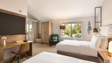 A hotel room with a desk, two beds, a chair, a view of the outdoors, and a large window.