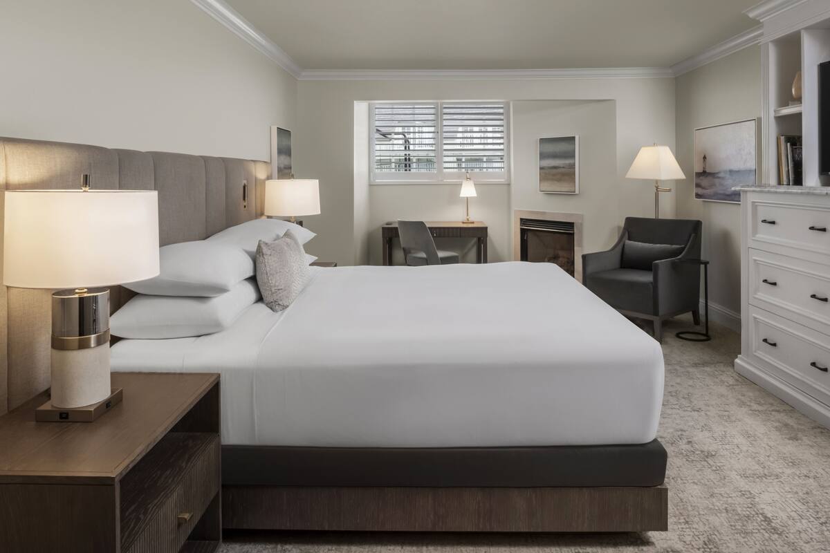 Una habitación de hotel moderna con una cama grande, lámparas de noche, un escritorio y una silla.