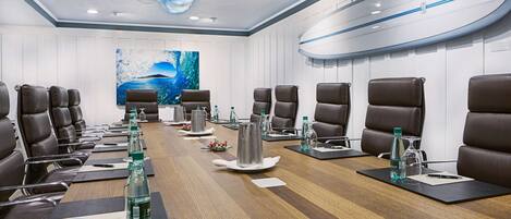 A conference room with a long wooden table, brown leather chairs, water bottles, and a surfboard decoration on the wall.
