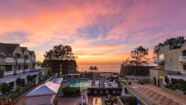 A resort with a pool, lounge chairs, and a view of the ocean at sunset.