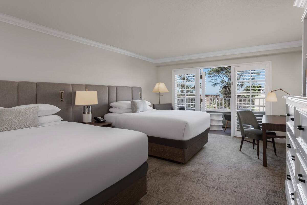 Habitación de hotel con dos camas, un escritorio y una silla. Cuenta con un balcón y vistas al exterior.