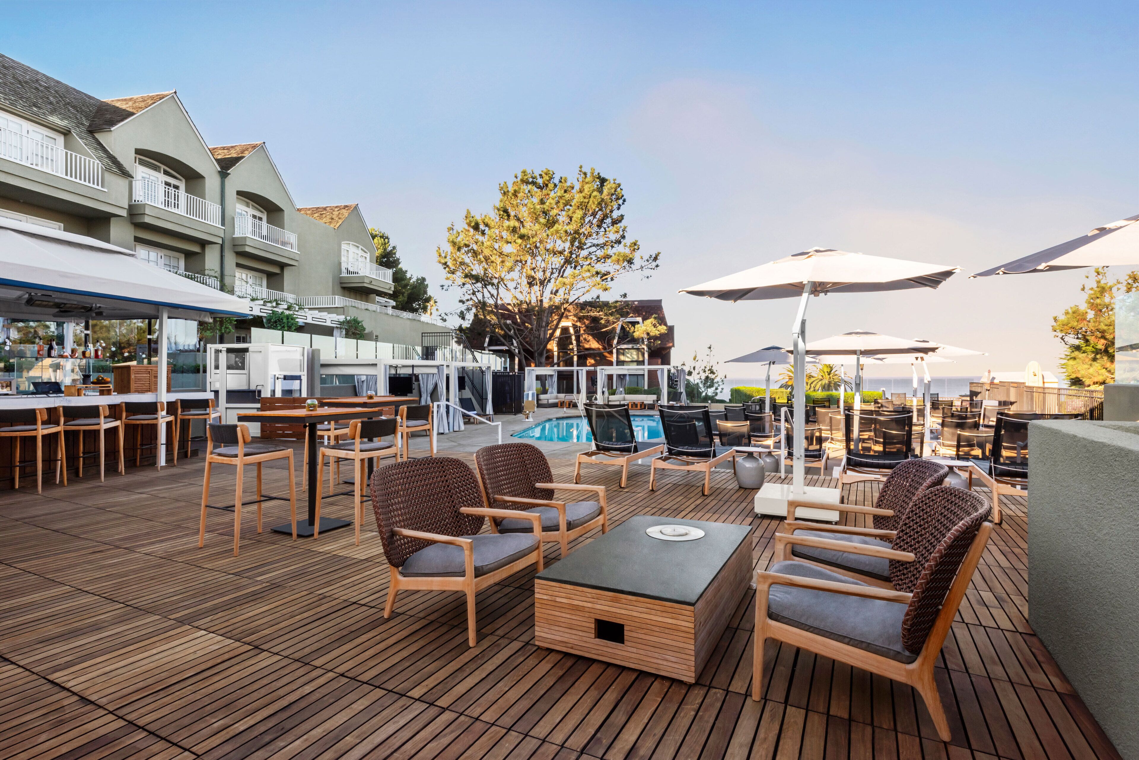A wooden deck with outdoor seating, a pool, and a building with balconies.