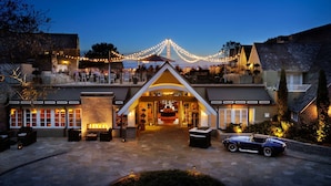 A large, modern house with a spacious outdoor area, a fire pit, and a classic car parked in front.