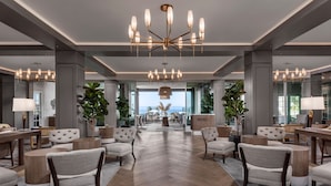 A spacious lobby with modern furniture, chandeliers, and large windows offering a view of the outdoors.
