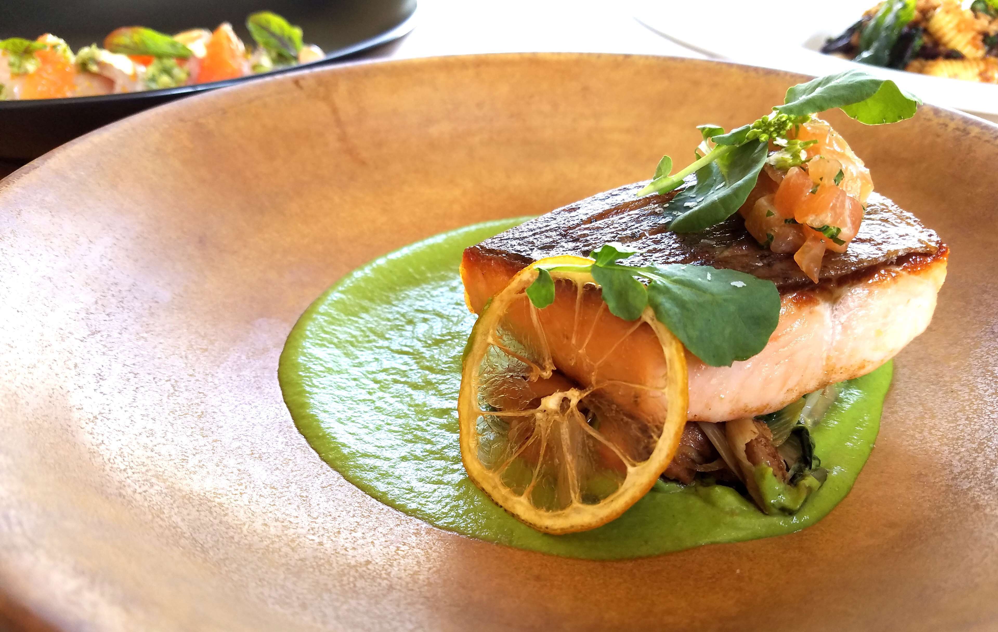 A dish with salmon, lemon, and greens on a plate.