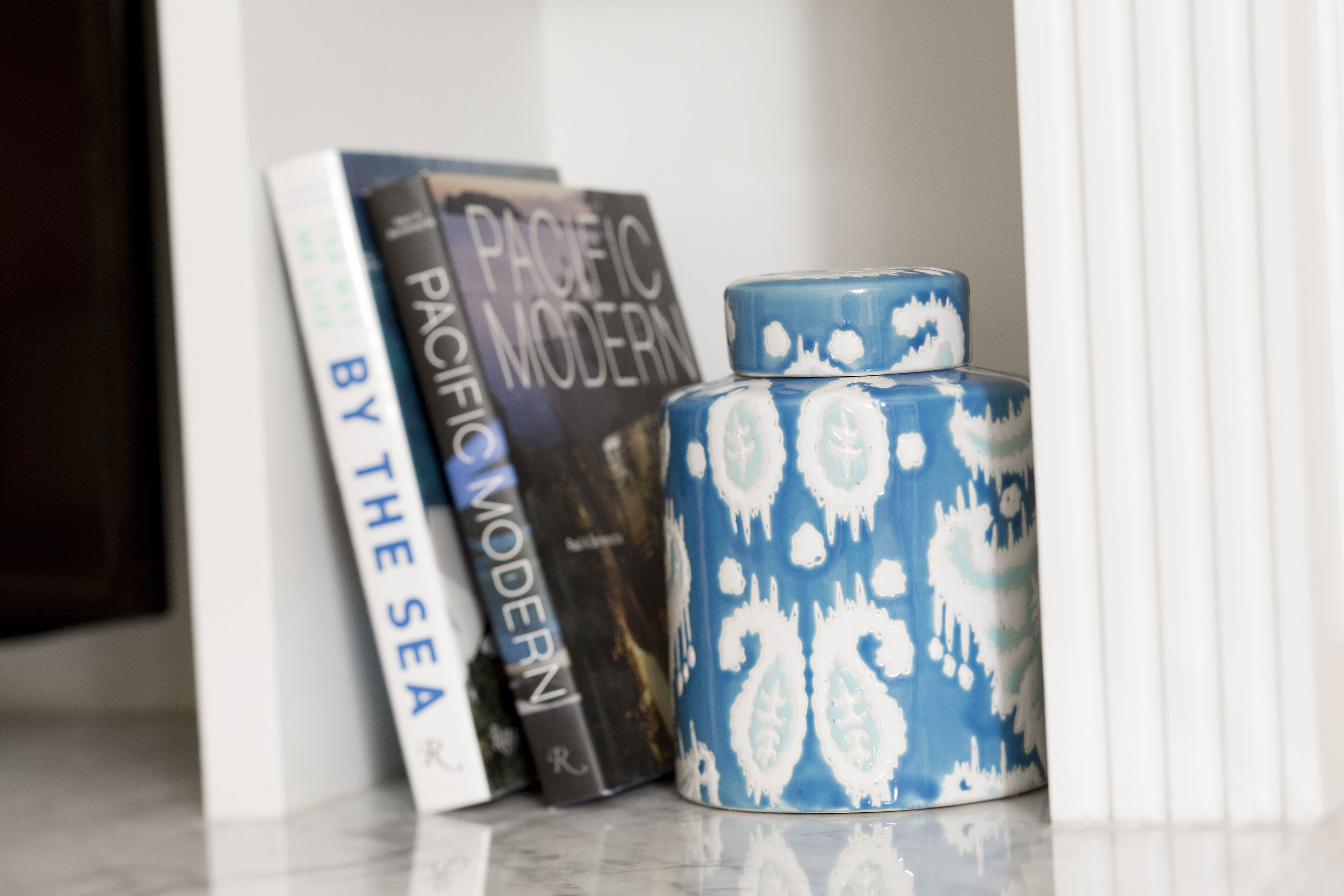 A bookshelf with books and a decorative blue and white ceramic container.