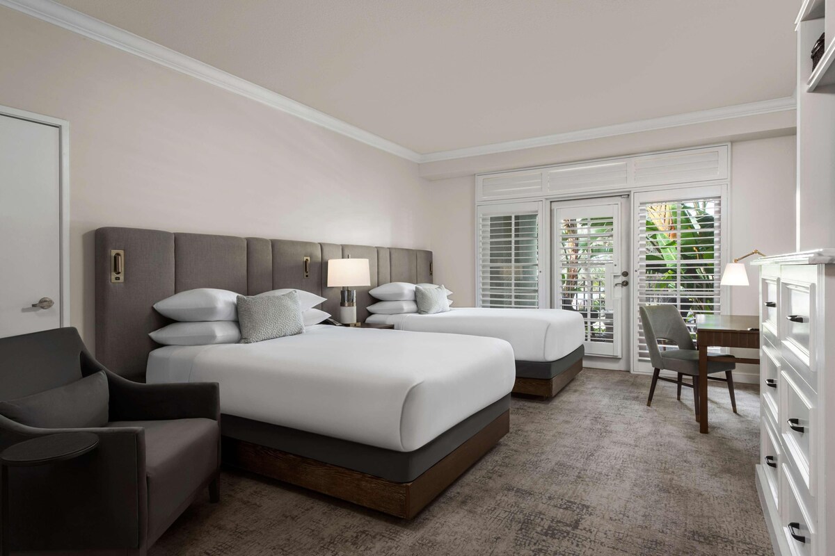 A hotel room with two beds, a desk, a chair, and a dresser.