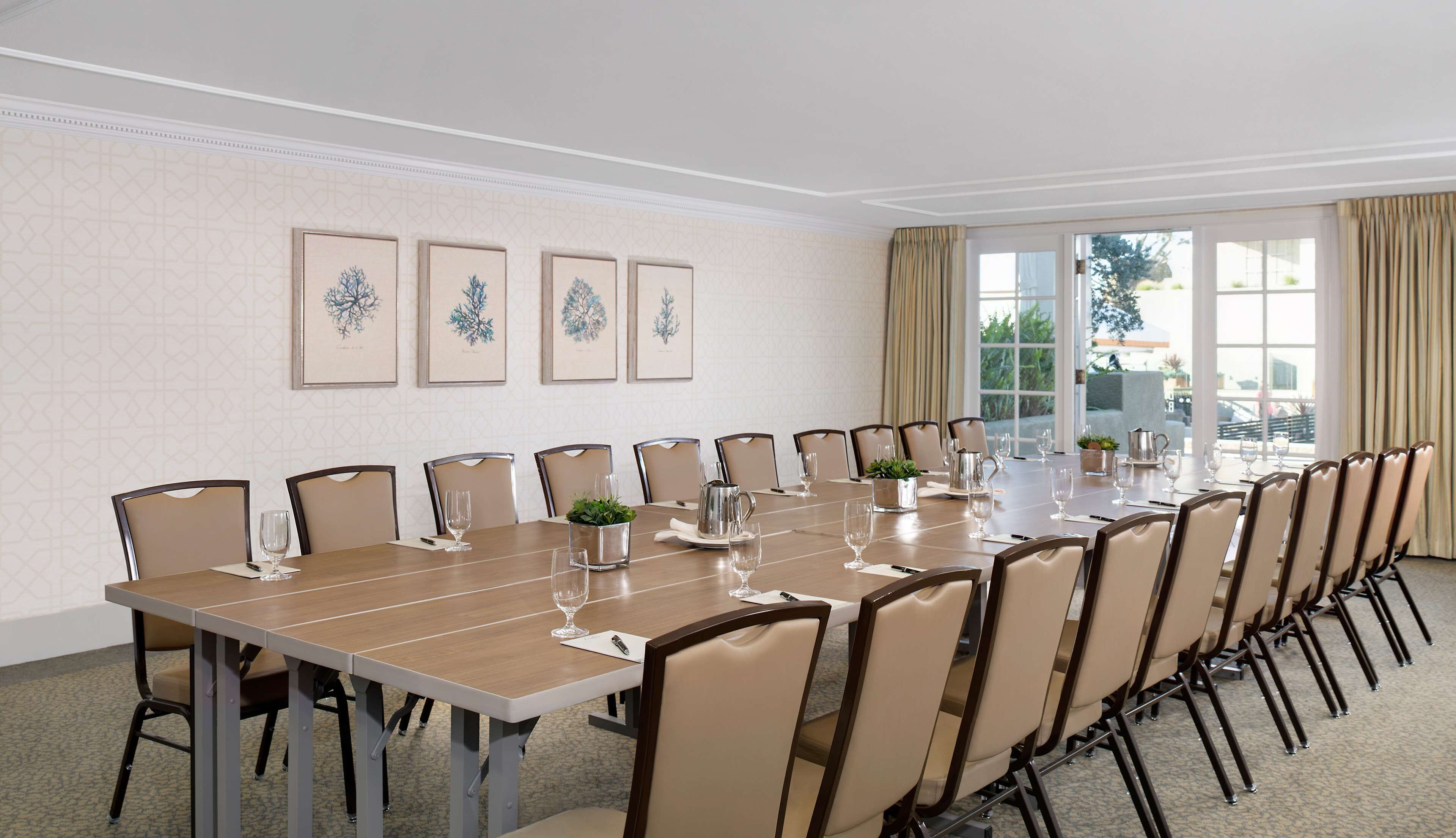 A conference room with a long table, chairs, framed botanical prints on the wall, and a view through large windows.