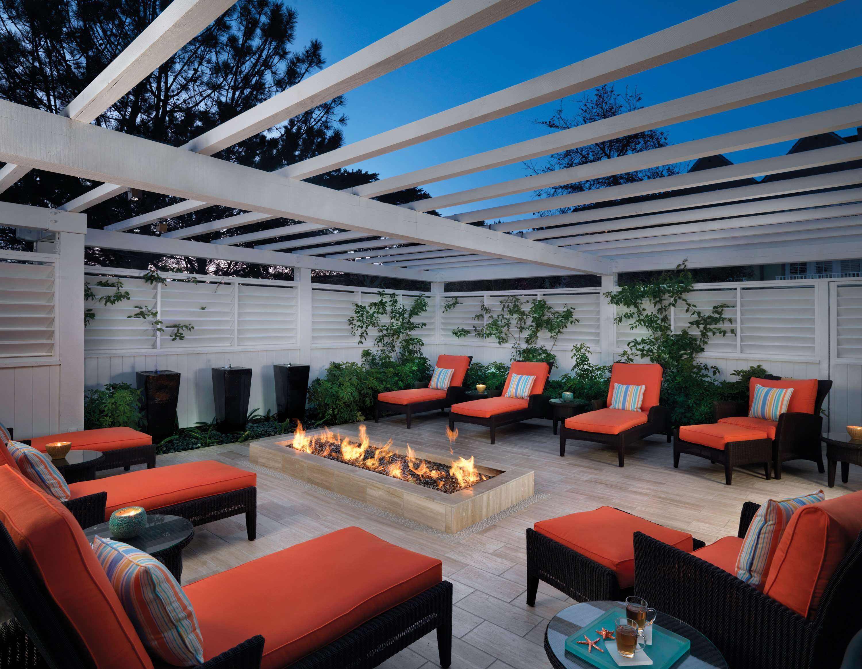 An outdoor patio area with a fire pit, multiple seating options including sofas and chairs, and a pergola structure.