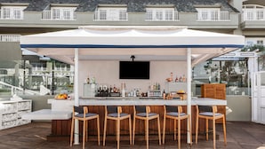 An outdoor bar area with a white counter, wooden chairs, and a TV screen.