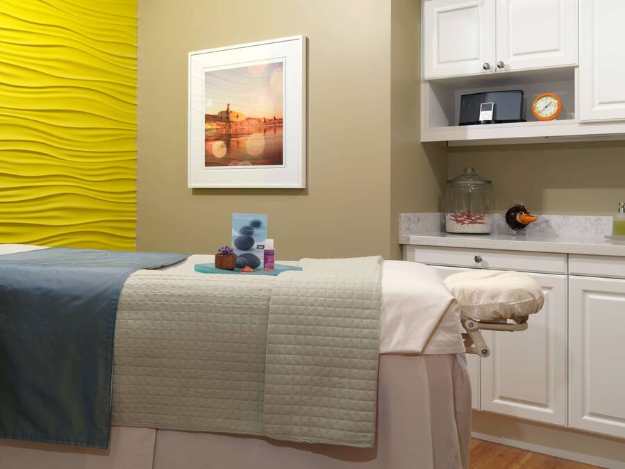 A room with a bed, a bedside table with a clock, a framed picture on the wall, and a yellow textured wall.