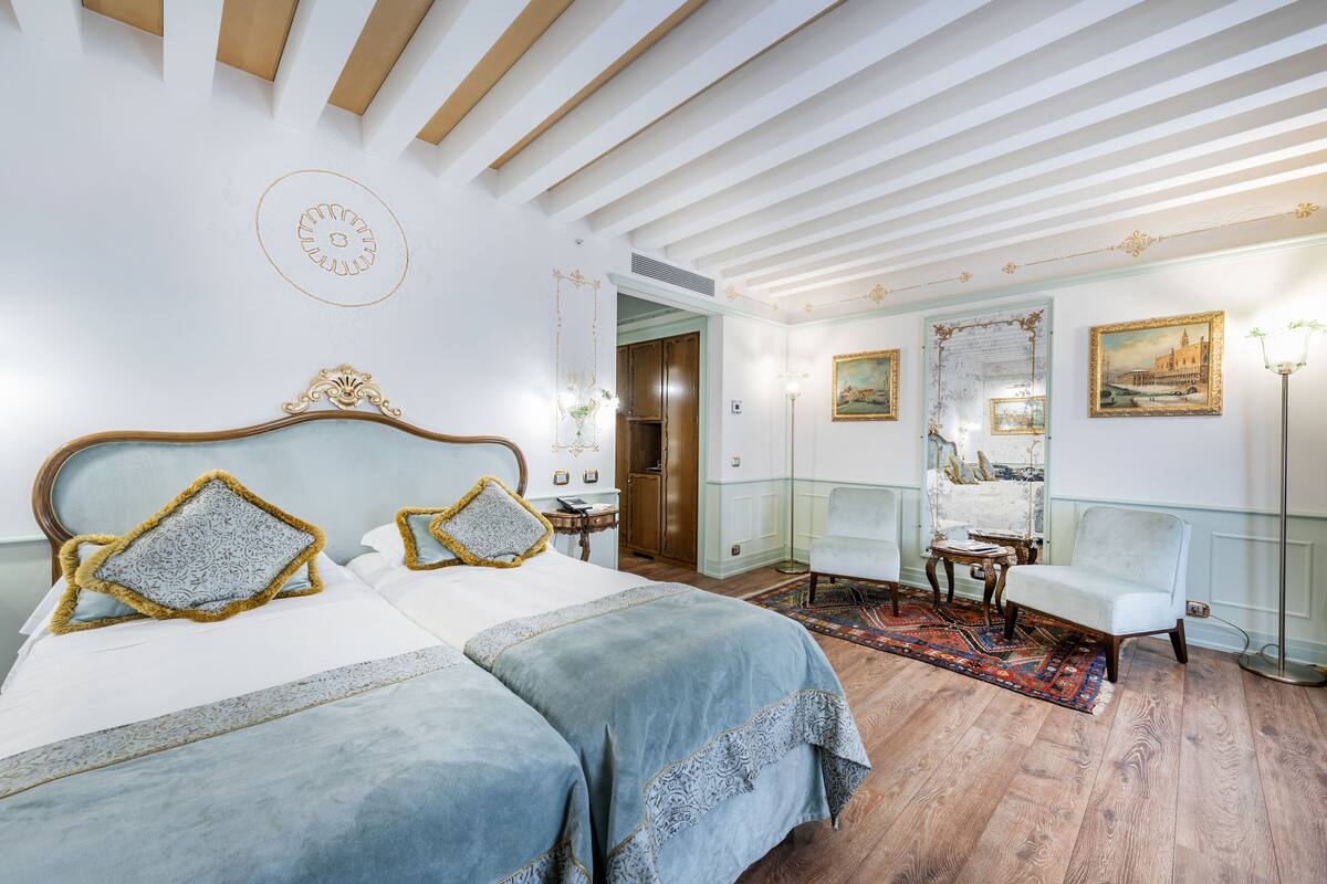 A hotel room with a large bed, a chair, a table, and a mirror.