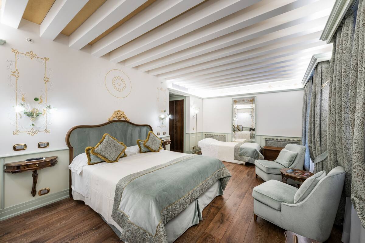 A spacious bedroom with a large bed, two armchairs, a wooden nightstand, and a mirror.