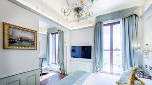 A hotel room with a large bed, a television, a painting of a cityscape, and a view of a body of water through the window. - Hotel Monaco & Grand Canal (Venice)