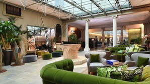 A spacious lobby with green sofas, a large mirror, and a bookshelf. - Hotel Monaco & Grand Canal (Venice)