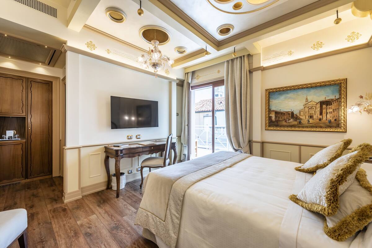 A hotel room with a large bed, a desk, a television, and a painting on the wall.