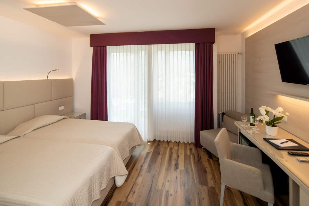 Ein Hotelzimmer mit zwei Betten, einem Schreibtisch mit Stuhl, einem Fernseher und einem Fenster mit Vorhängen.