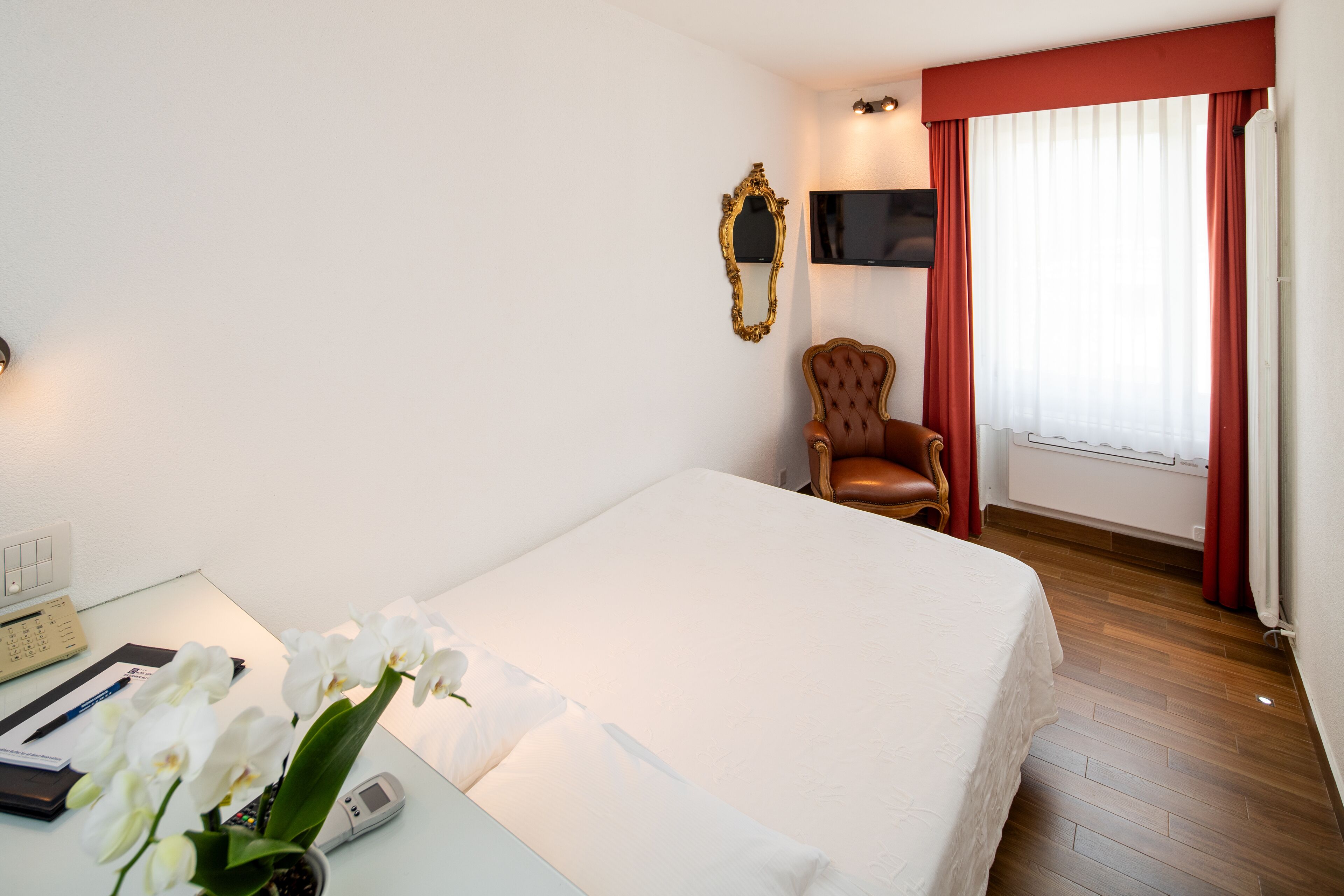 Habitación de hotel con cama, escritorio con teléfono, silla, televisor y ventana con cortinas.