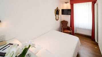 Habitación de hotel con cama, escritorio con teléfono, silla, televisor y ventana con cortinas.