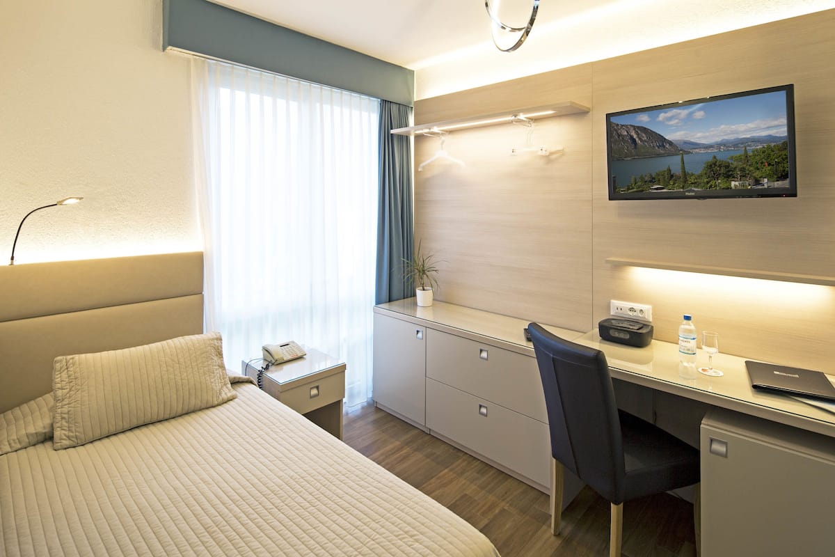 Ein Hotelzimmer mit Bett, Schreibtisch, Stuhl und einem an der Wand befestigten Fernseher.