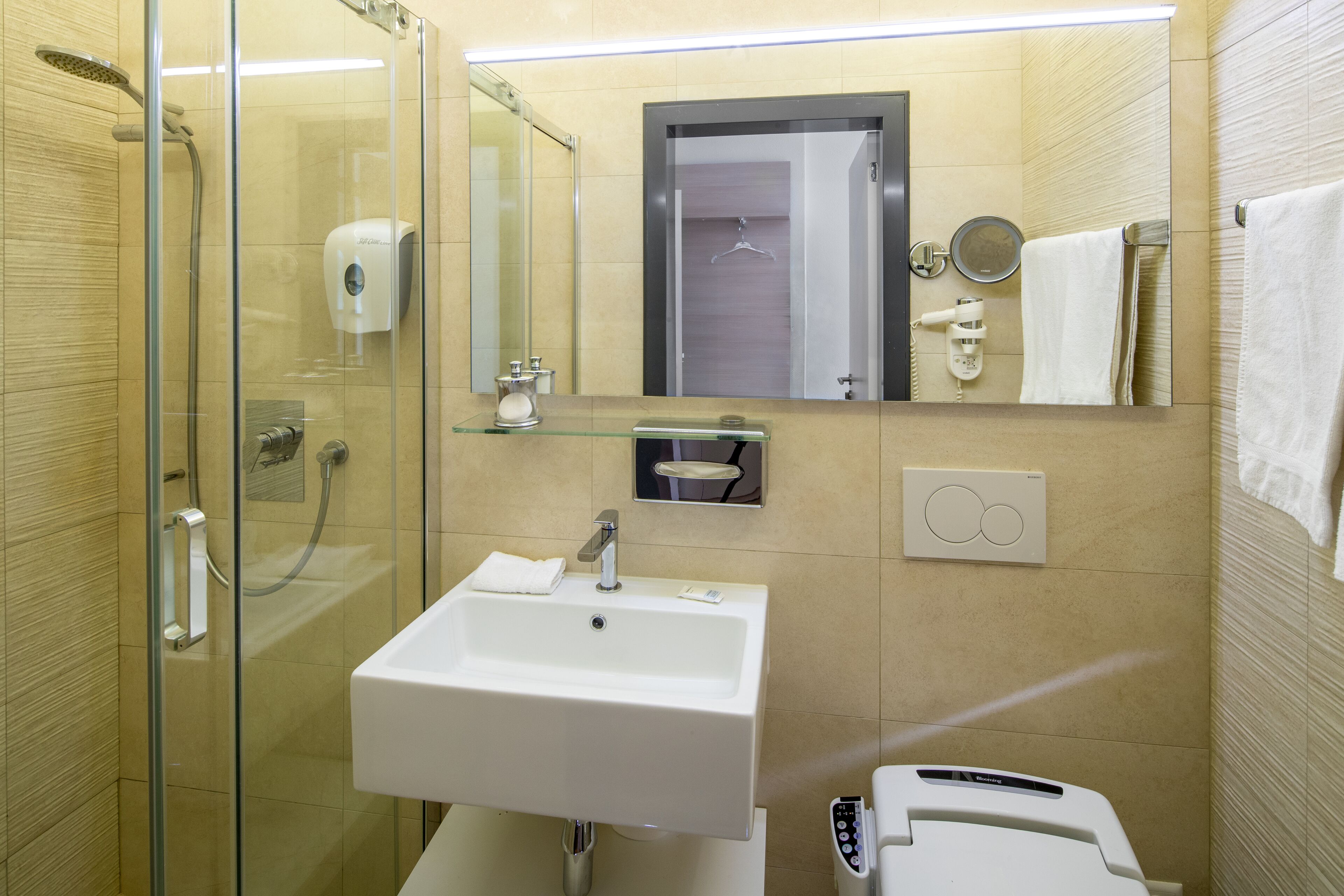 A modern bathroom with a glass-enclosed shower, a white sink, a mirror, and a towel rack.