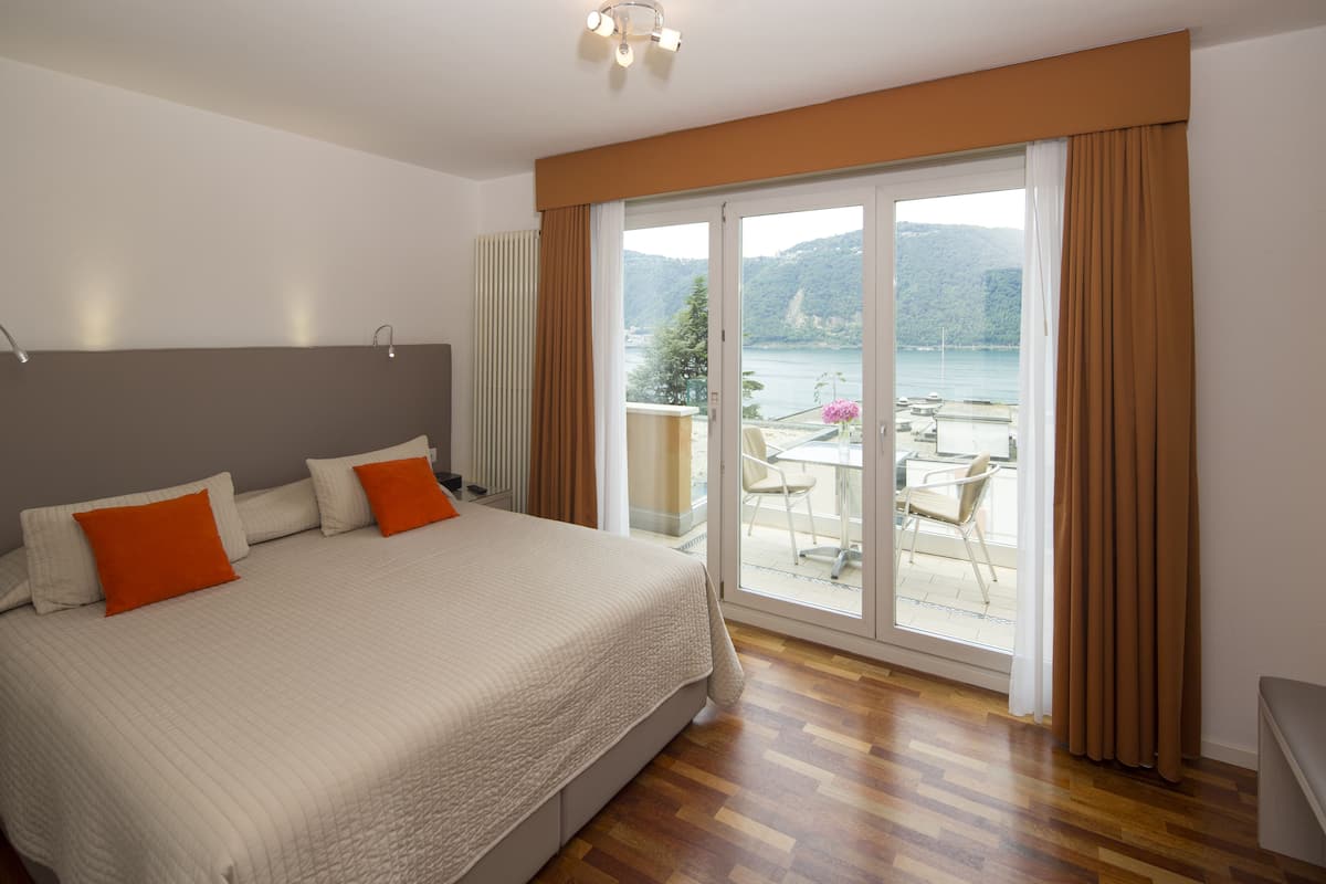 Ein Schlafzimmer mit einem großen Bett, Blick auf einen Balkon mit Gartenmöbeln und eine schöne Seenlandschaft.