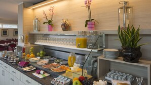 Un bufé de desayuno con diversos alimentos, cristalería y plantas decorativas.