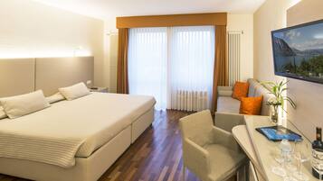 A hotel room with a large bed, a desk with a chair, a flat-screen TV, and a view of the outdoors through the window.