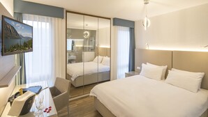 Habitación de hotel con una cama grande, un escritorio con una computadora y una botella de champán, un televisor montado en la pared y vistas de la montaña a través de la ventana.