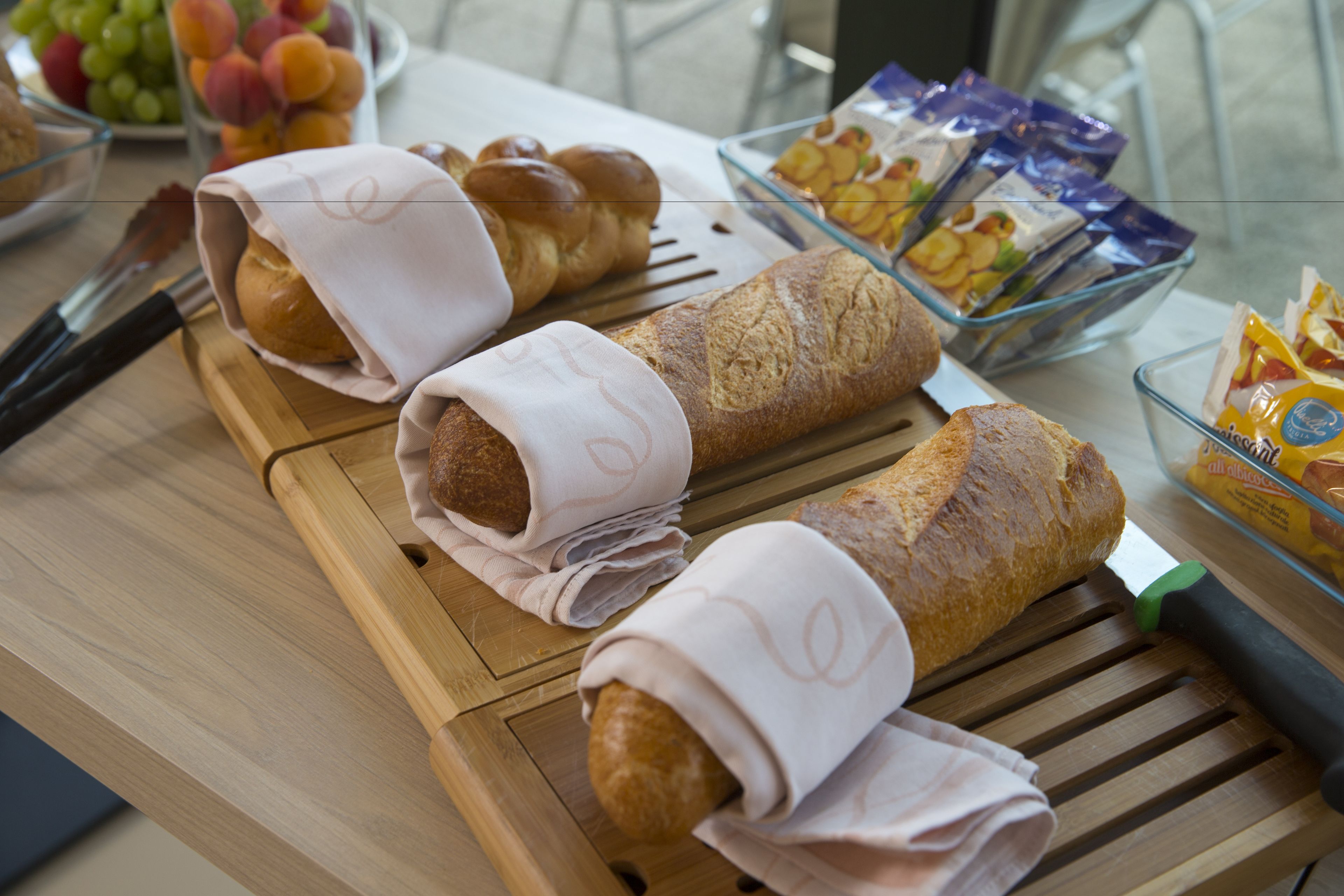 A table with bread rolls, a knife, and a bowl of fruit.