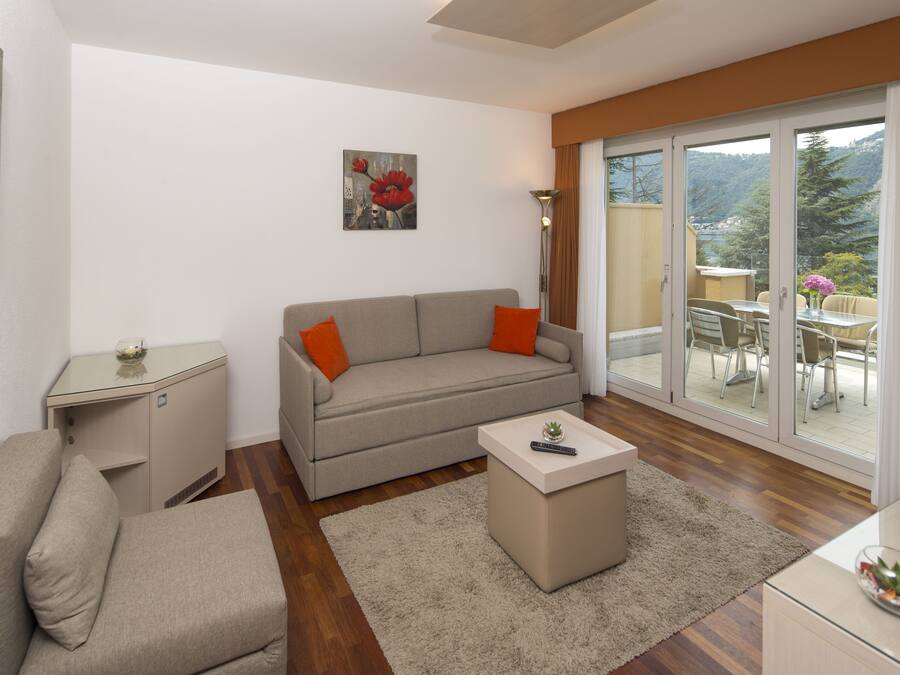Una sala moderna con un sofá, una mesa de centro y una mesita auxiliar. Hay una puerta corrediza de vidrio que da a un área exterior con una mesa y sillas.