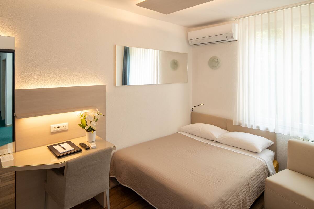 Ein Hotelzimmer mit einem Bett, einem Schreibtisch mit Lampe, einem Spiegel und einer Klimaanlage.
