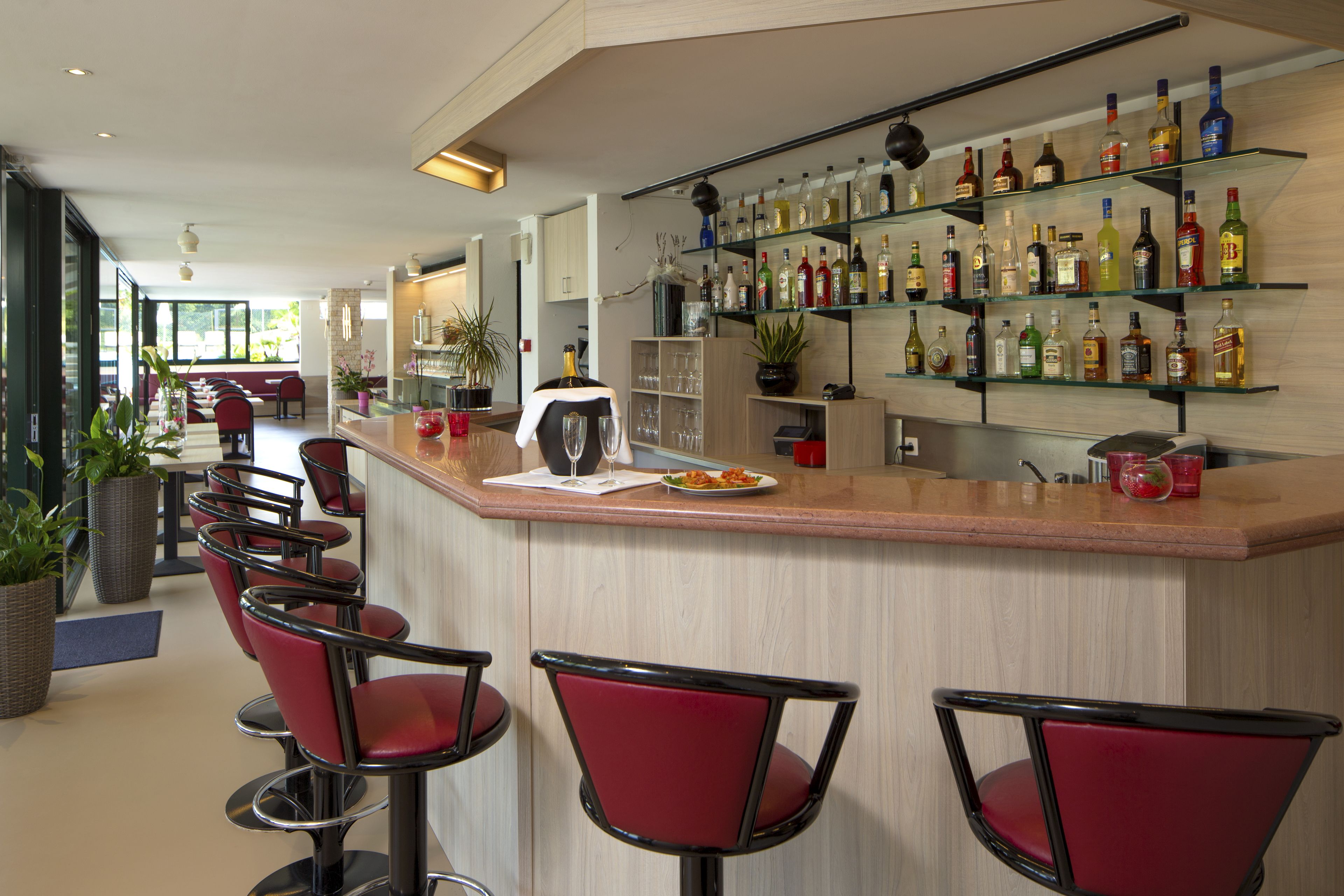 A bar area with red bar stools, a countertop with a glass, and shelves with various bottles.