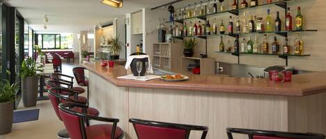 A bar area with red bar stools, a countertop with a glass, and shelves with various bottles.
