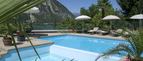 Una piscina con vistas a las montañas, rodeada de sillas de descanso y sombrillas.