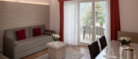 A modern living room with a grey sofa, red cushions, a small table with a vase of flowers, and a dining area with a table set for two.