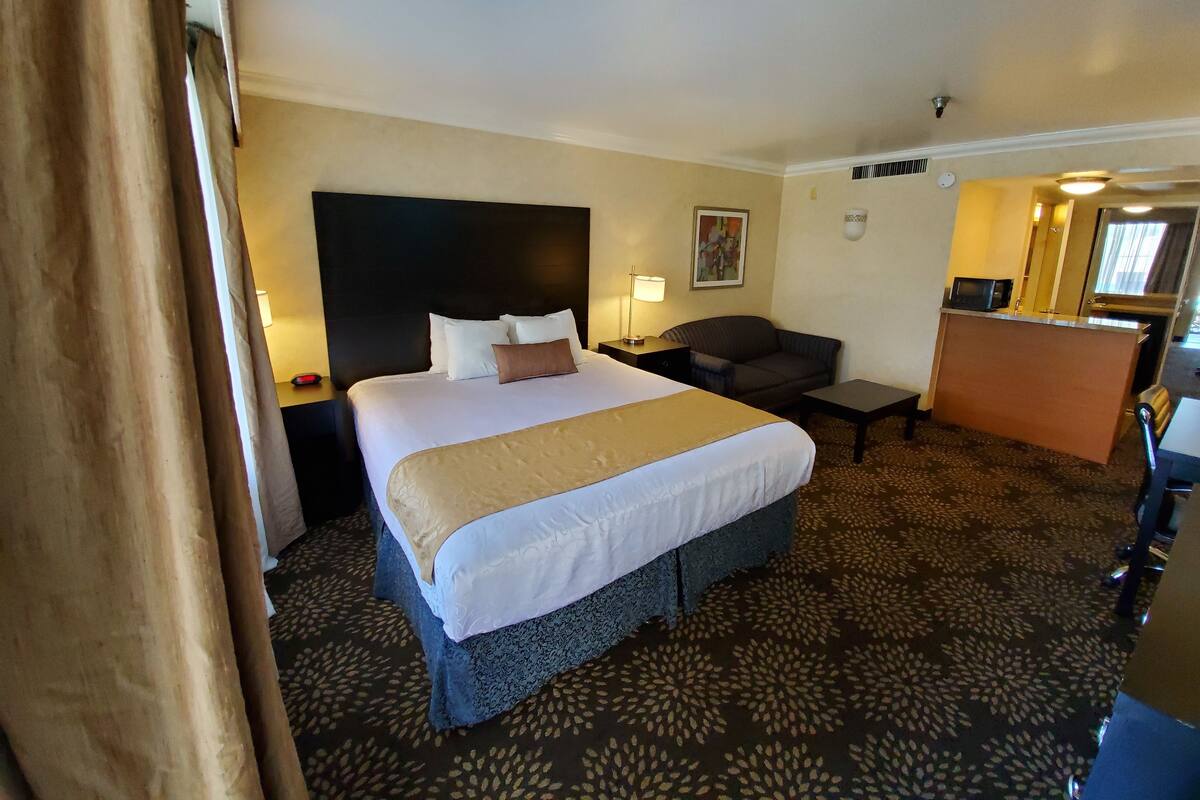 A hotel room with a large bed, a desk, a chair, a sofa, a small table, and a bathroom area.