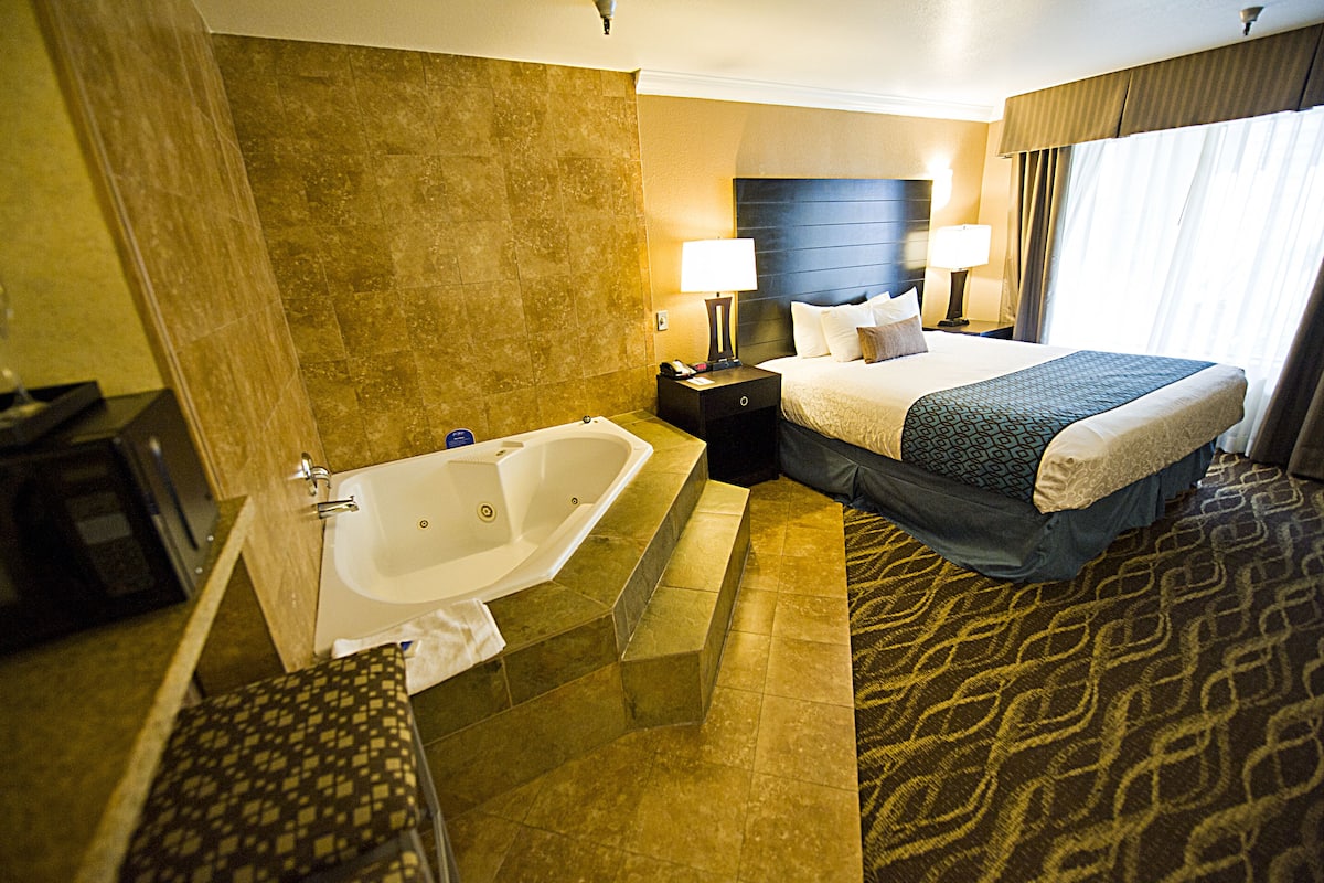 A hotel room with a large bed, a separate bathroom with a bathtub, and a patterned carpet.
