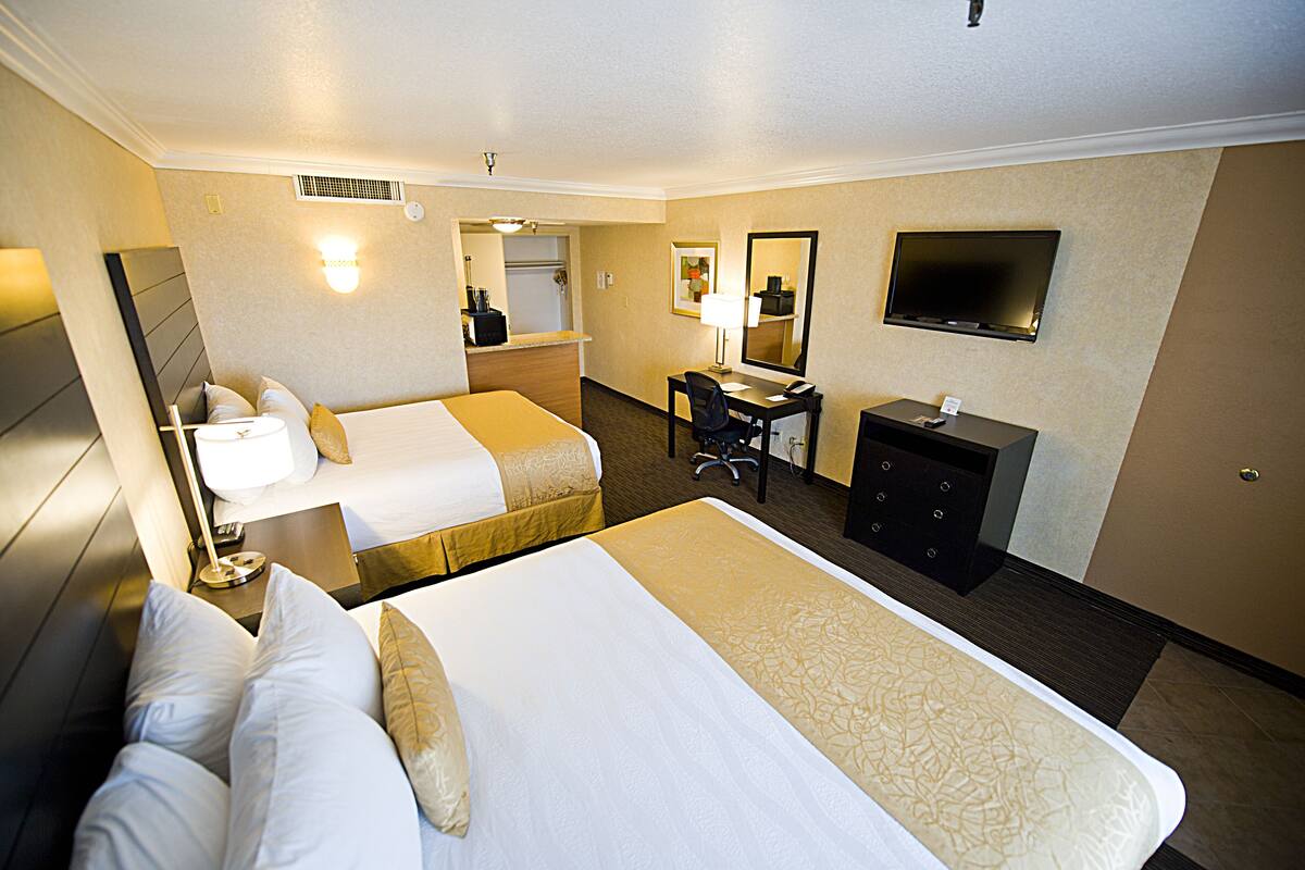 A hotel room with two beds, a desk, a chair, a TV, and a mirror.